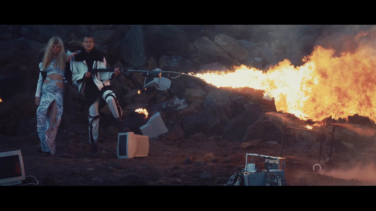 Zebra Katz and Leila beside burning computer monitors in the You Tell Em video
